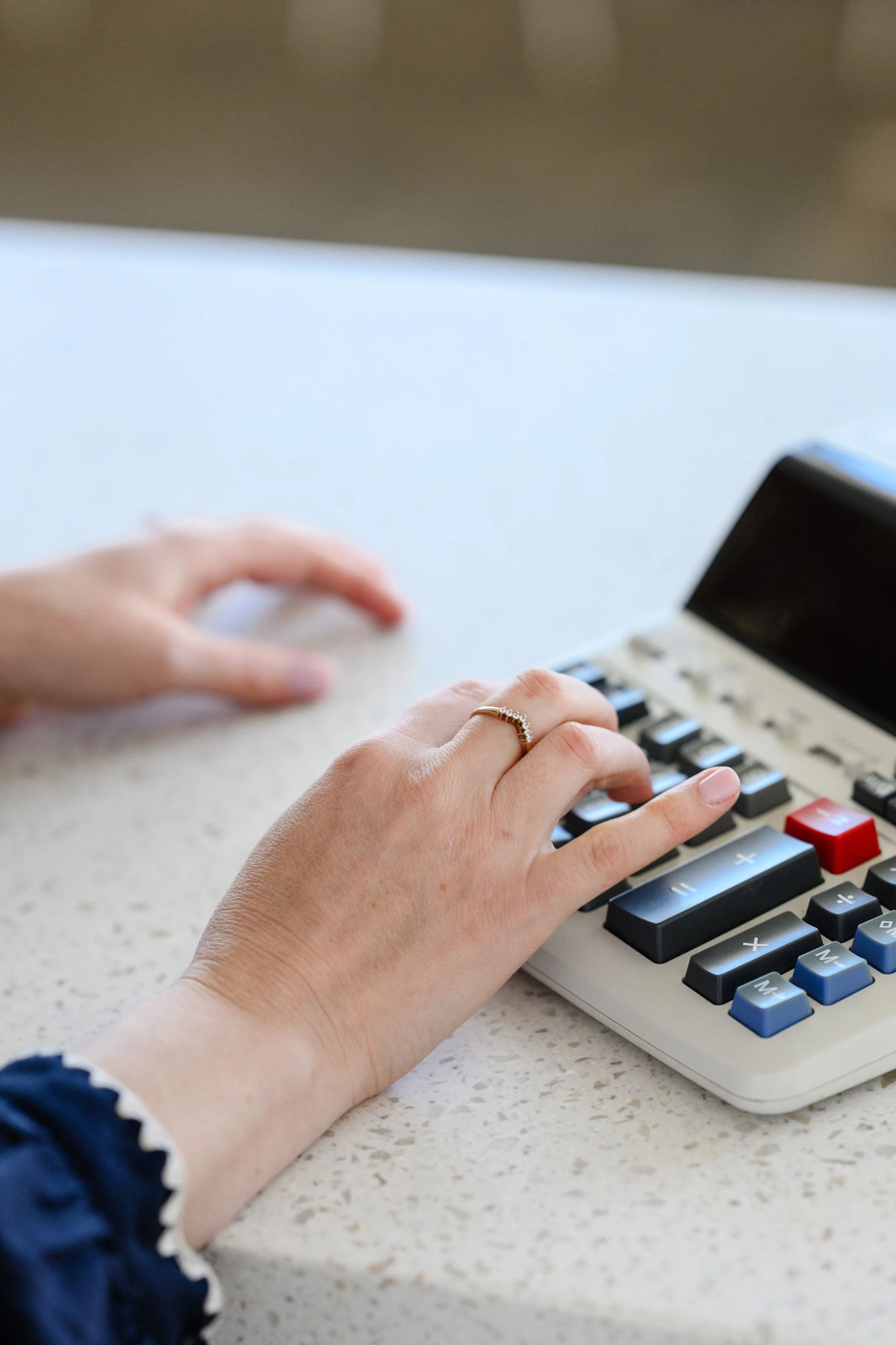 A person's hands typing on a computer keyboard with a calculator nearby on a desk.
