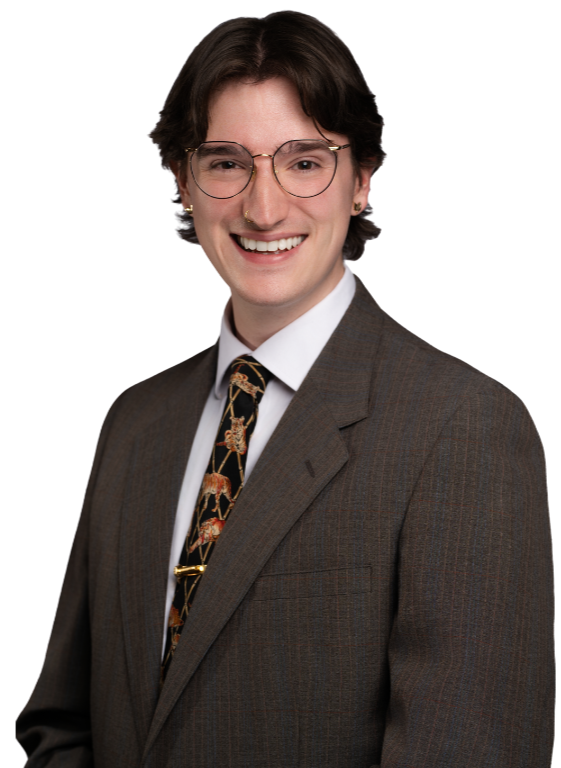 A young person with short dark hair, glasses, and a big smile, wearing a dark brown suit, white shirt, and patterned tie with animals on it.