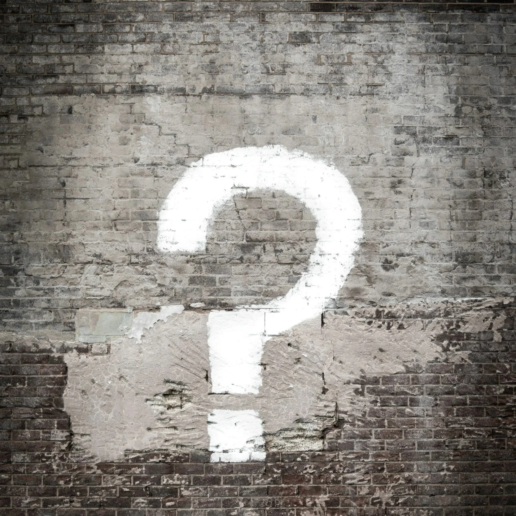 A brick wall with a painted white question mark.