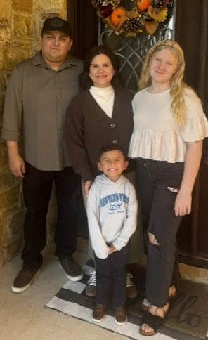 Family of four standing indoors in front of a Halloween-themed decoration, including a man, a woman, a teenage girl, and a young boy.