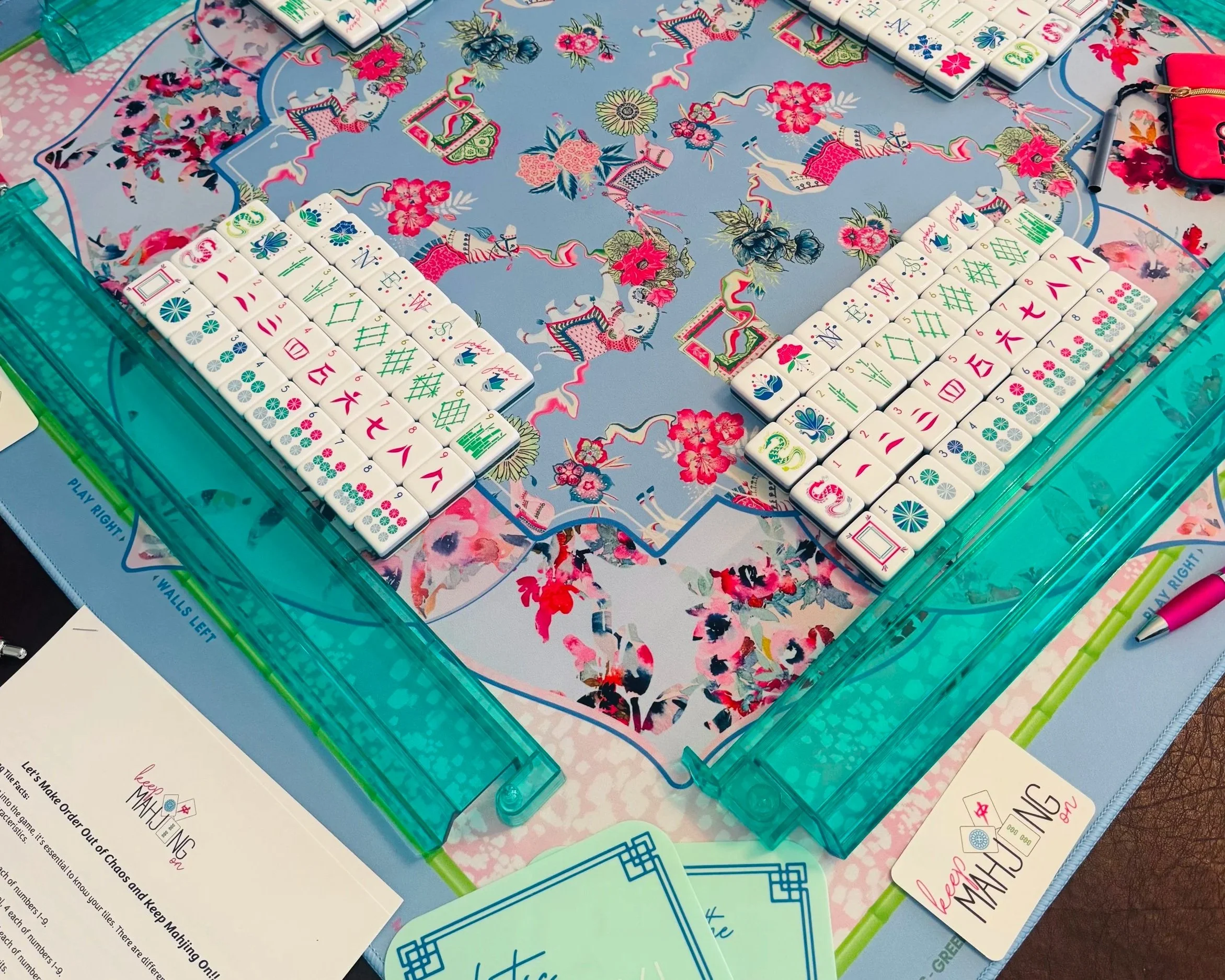 A colorful mahjong mat with floral and dragon designs, surrounded by mahjong tiles and game accessories.
