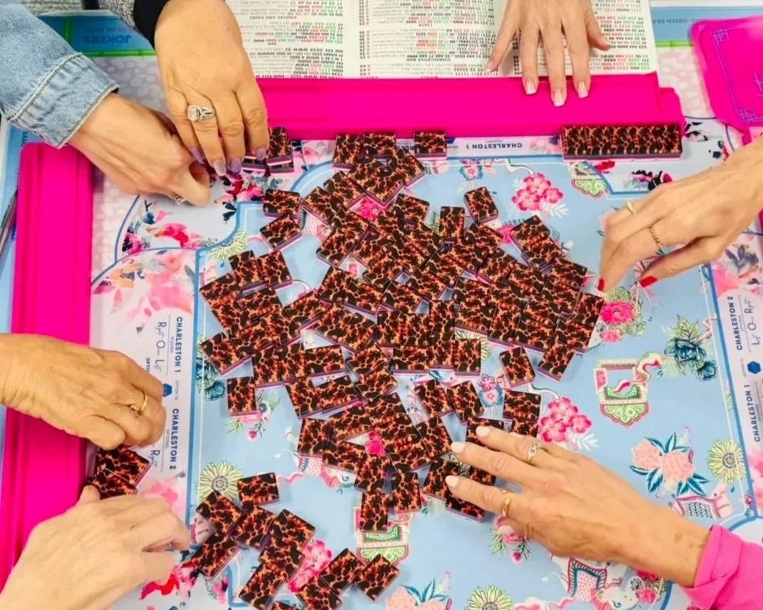 Four people playing mahjong on a colorful mahjong mat, with many mahjong tiles featuring a leopard print pattern on a pink frame.