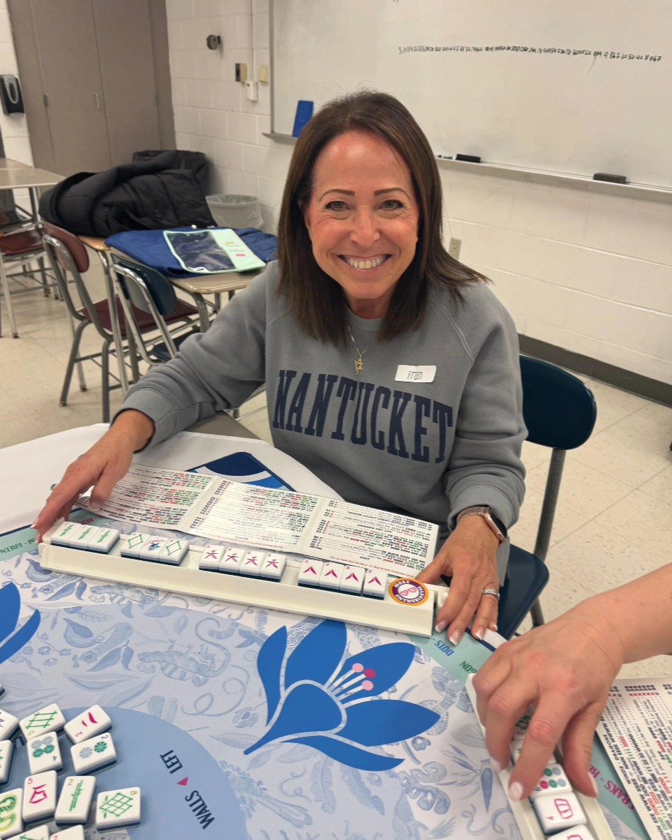Woman smiling and playing Mahjong at a table in a classroom setting.
