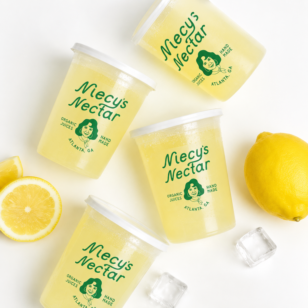 Four cups of Mely's Nectar lemon juice with lemon halves, a lemon, and ice cubes on white background.