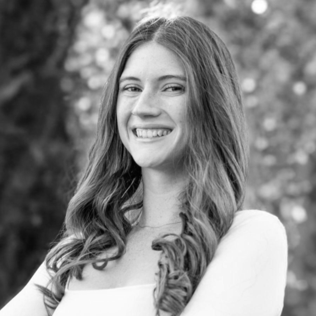 Black and white photo of a young woman with long curly hair smiling outdoors.