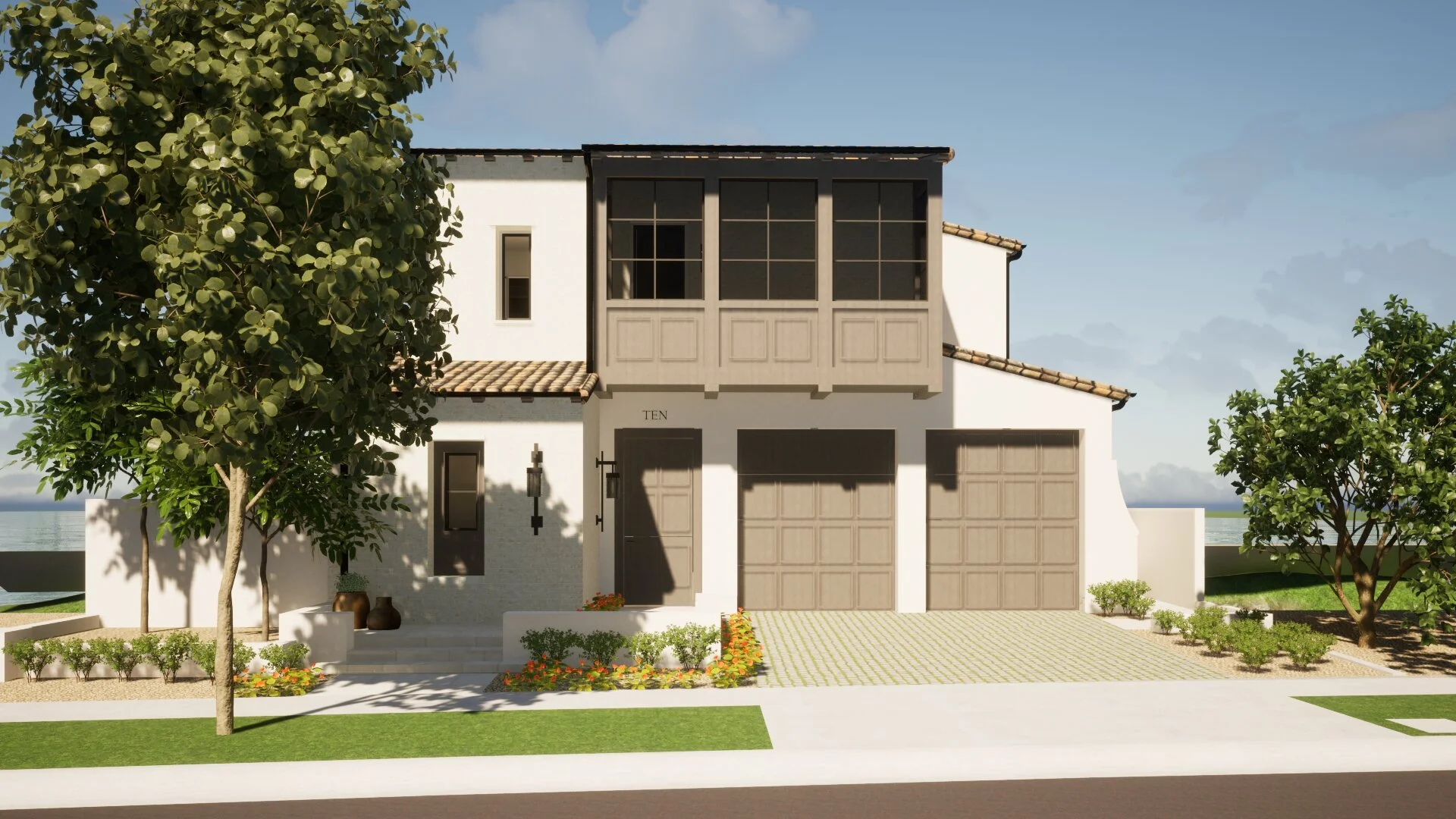 A modern two-story house with white exterior walls, a tiled roof, and a balcony with black framing. The house has a small front porch with potted plants, a pathway, and a landscaped yard with trees, bushes, and flowers. The sky is partly cloudy with a view of water in the background.