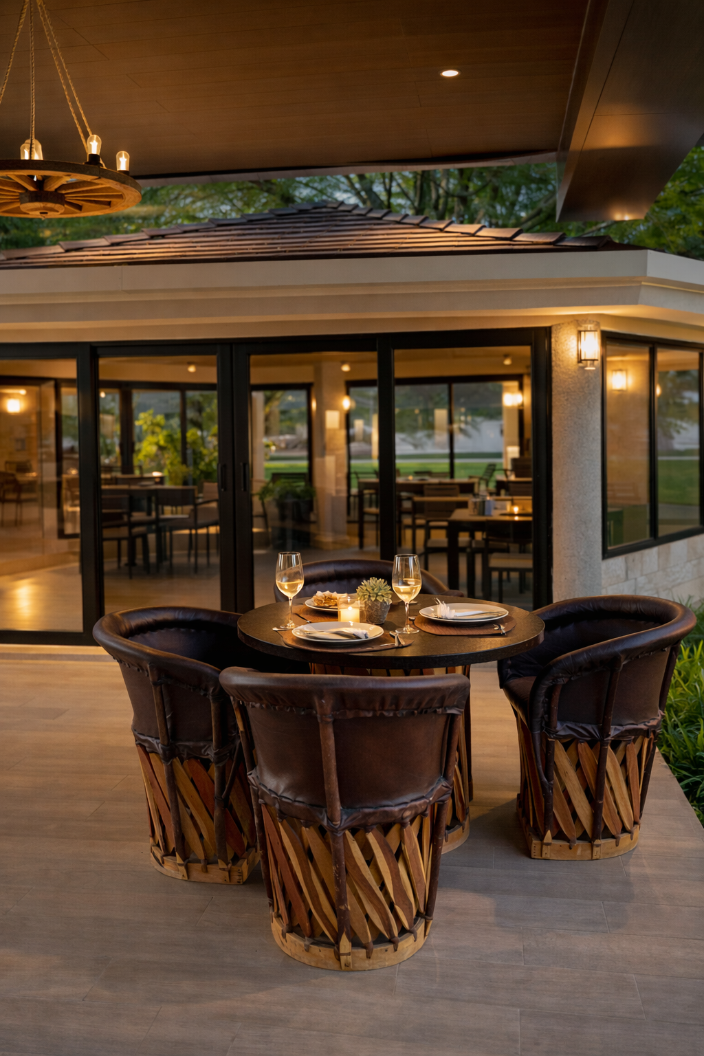 Mesa para dos personas con dos copas de vino, platos y velas, en un restaurante interior con ventanas de cristal y vista al exterior, decorado con luz cálida y plantas.