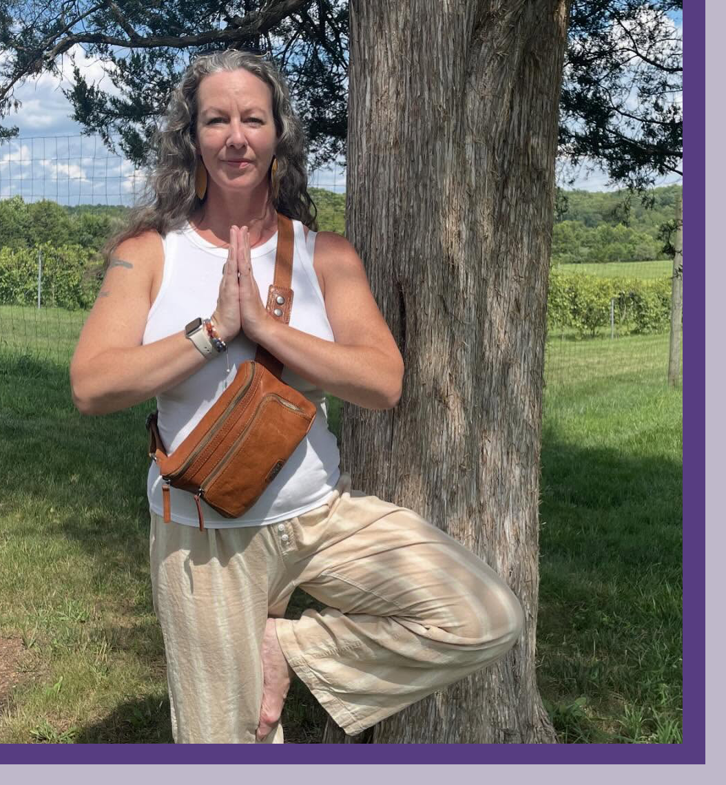 Trish outside in a simple yoga pose against a tree.