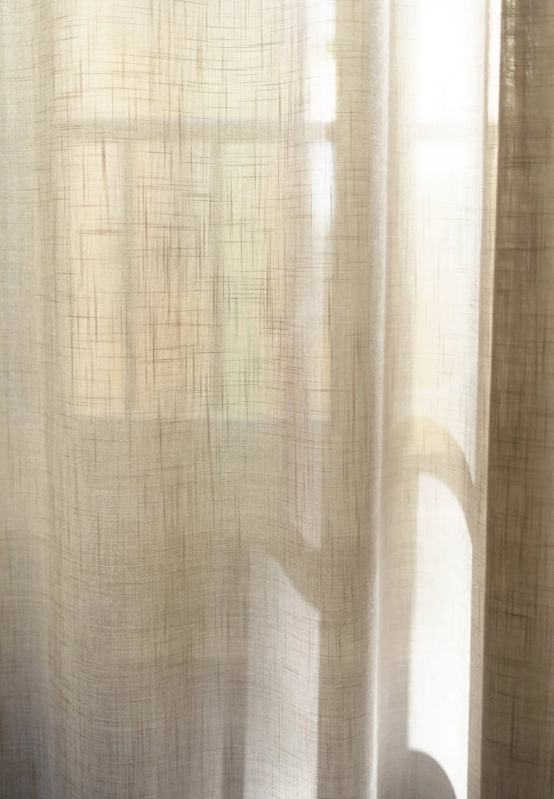 Close-up of a sheer beige curtain with a subtle checkered pattern, illuminated by sunlight.