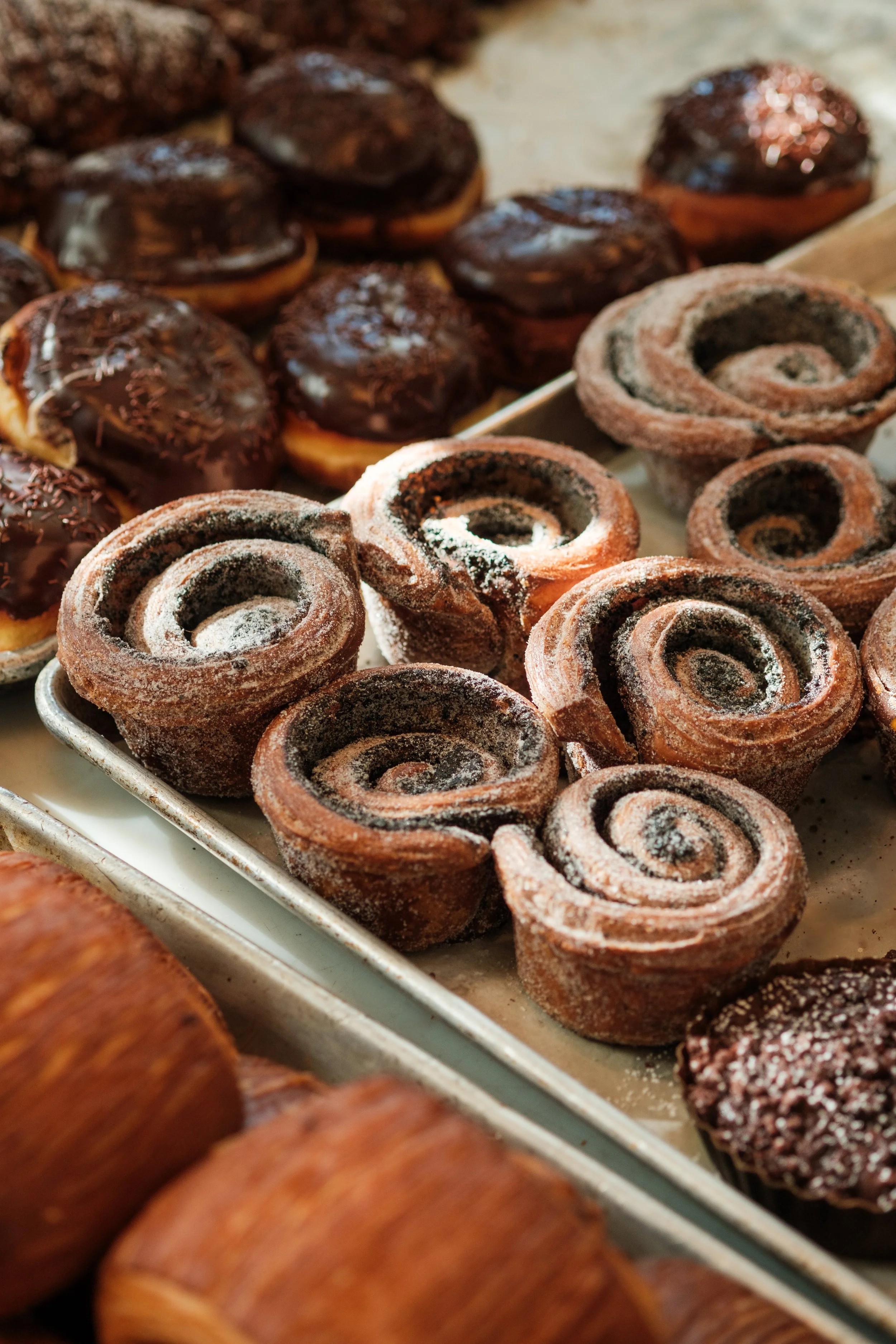 Donuts, morning buns, and assorted croissants lined up on baking trays by Krescent Carasso.