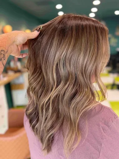 Side view of a woman with wavy, multi-tonal hair in a salon setting.