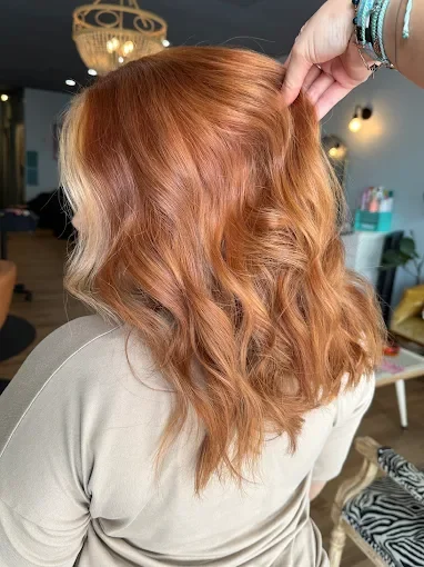 Person with wavy, copper-colored hair sitting in a salon or modern interior space.