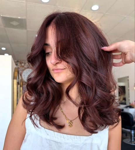 Woman with shoulder-length, wavy, auburn hair looking downward in a salon.
