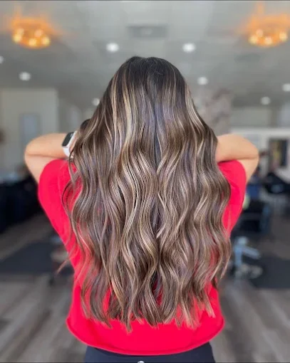 Back view of a woman with long, wavy, highlighted hair wearing a red top in an indoor setting.