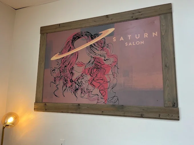 Artwork of a woman with long, curly hair, with a Saturn-like ring around her head, and the text "SATURN SALON" on a pink background.