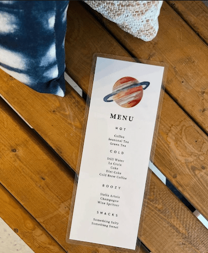 Cafe menu featuring hot, cold, boozy drinks, and snacks, with a planet illustration at the top.