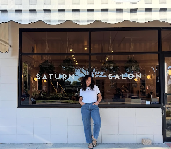 Woman standing outside Saturn Salon with large glass storefront window.