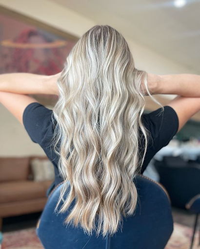 Back of a woman with long, wavy blonde hair sitting in a blue chair.