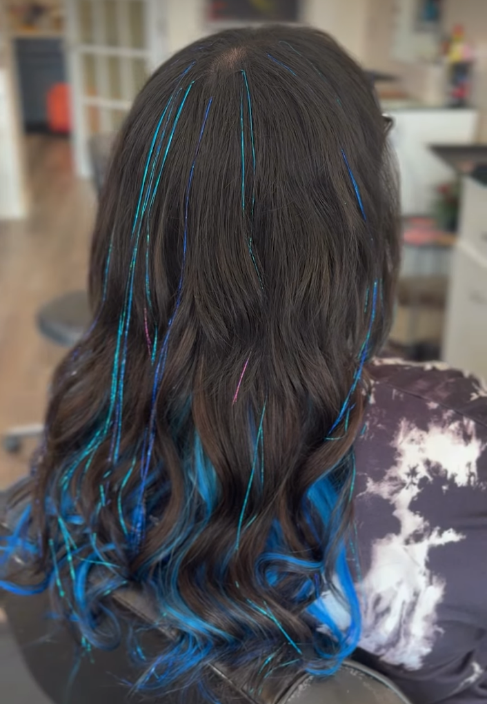 Woman's dark brown hair with blue streaks at a salon.