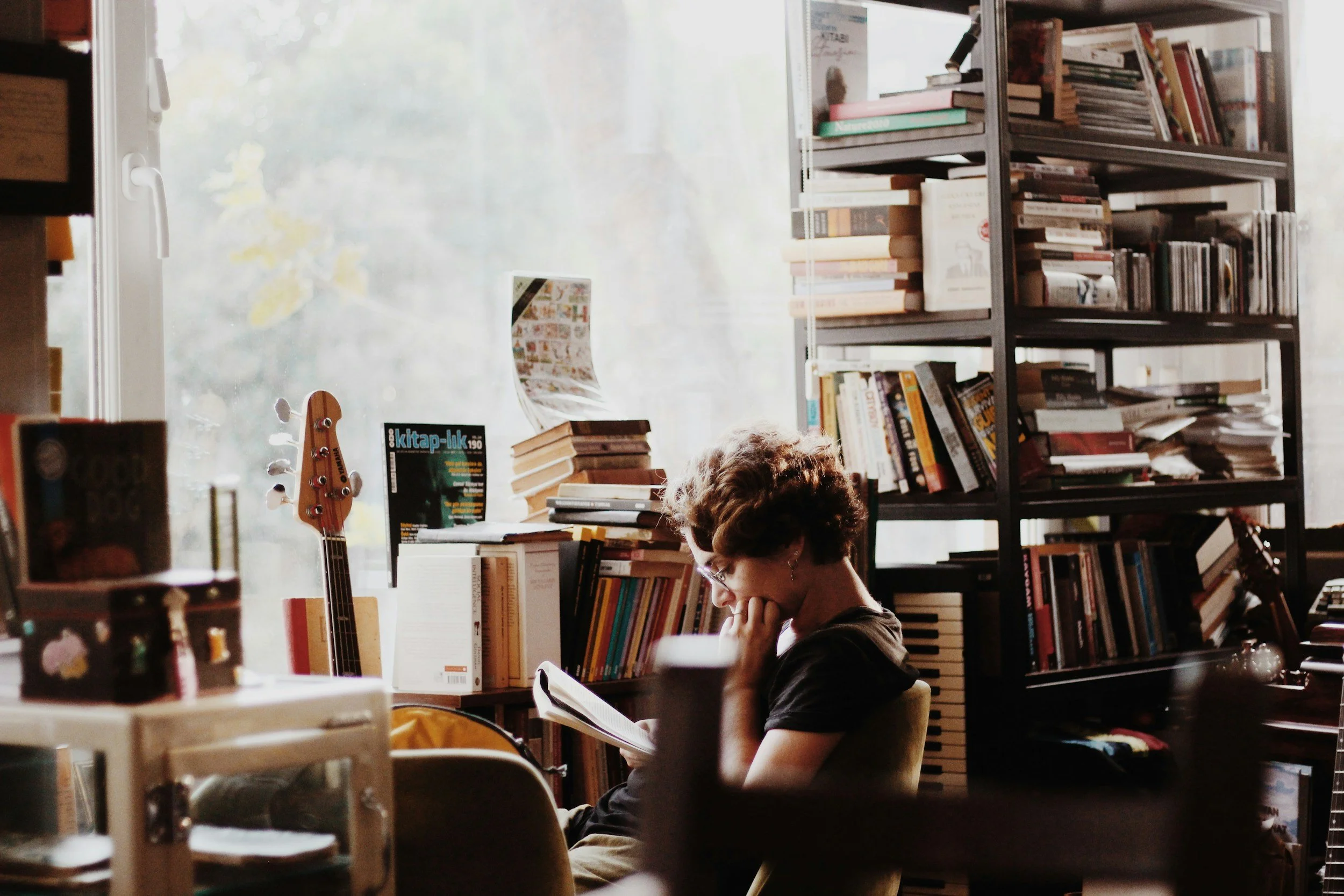 image of a person with curly hair reading peacefully, surrounded by books