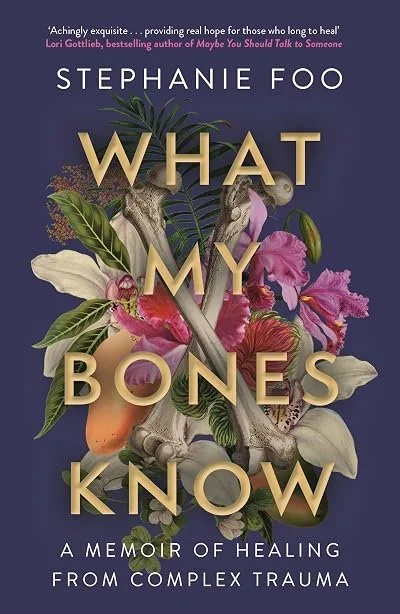 Book cover titled "What My Bones Know" by Stephanie Foo. The cover features a dark purple background with an arrangement of flowers, leaves, a chicken bone, and a human skull. The subtitle reads "A Memoir of Healing from Complex Trauma."