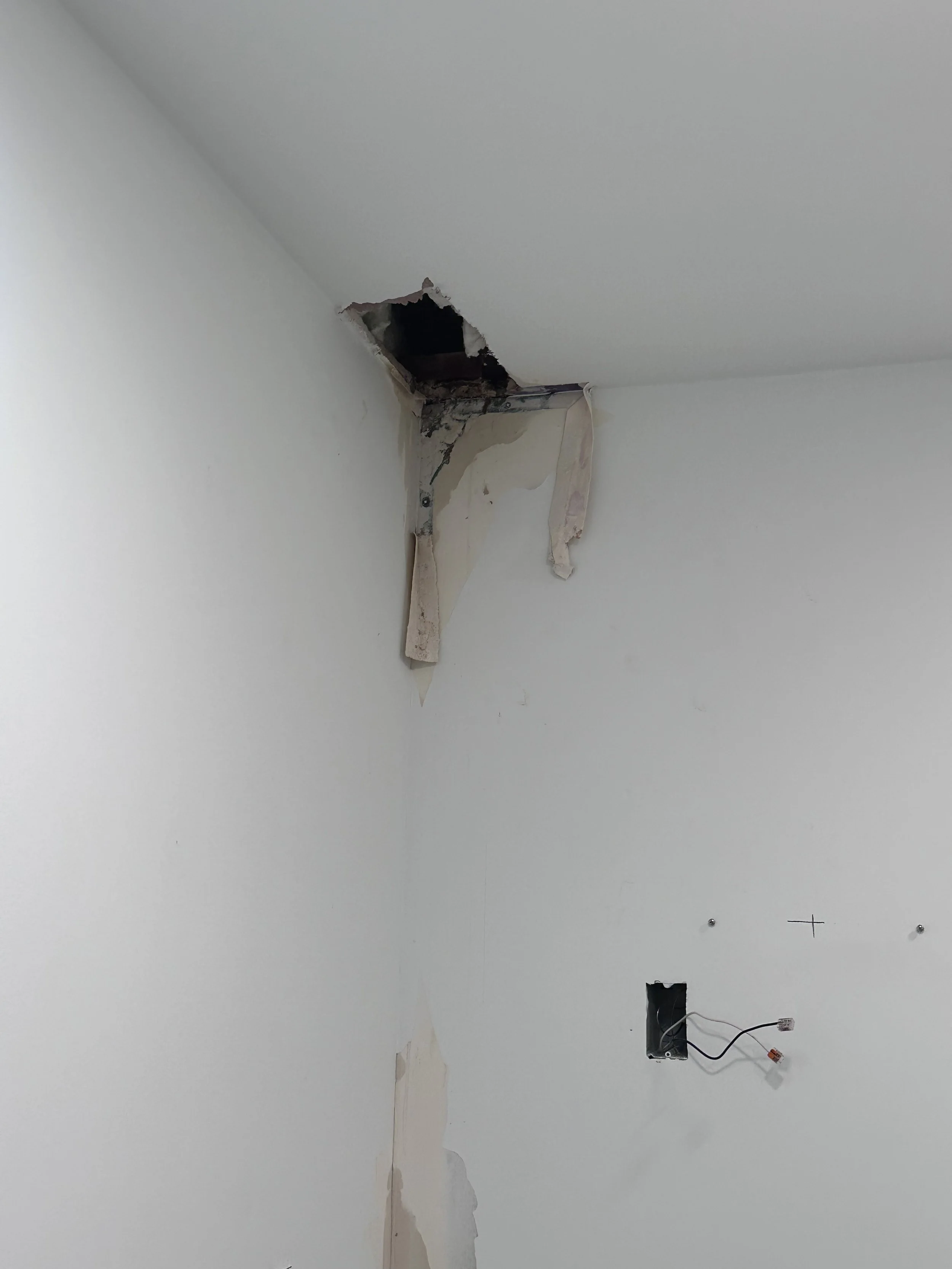 Living room wall with hole in ceiling and exposed wires.