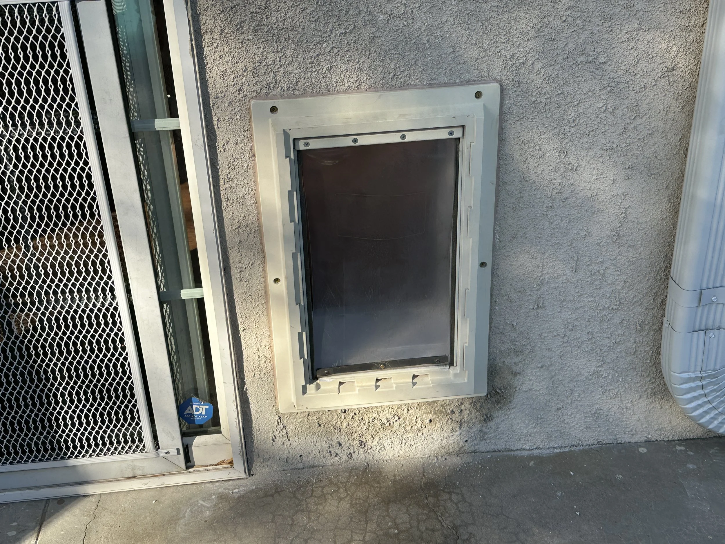An outdoor scene showing a worker opening an air conditioning or refrigeration unit on a light-colored wall.