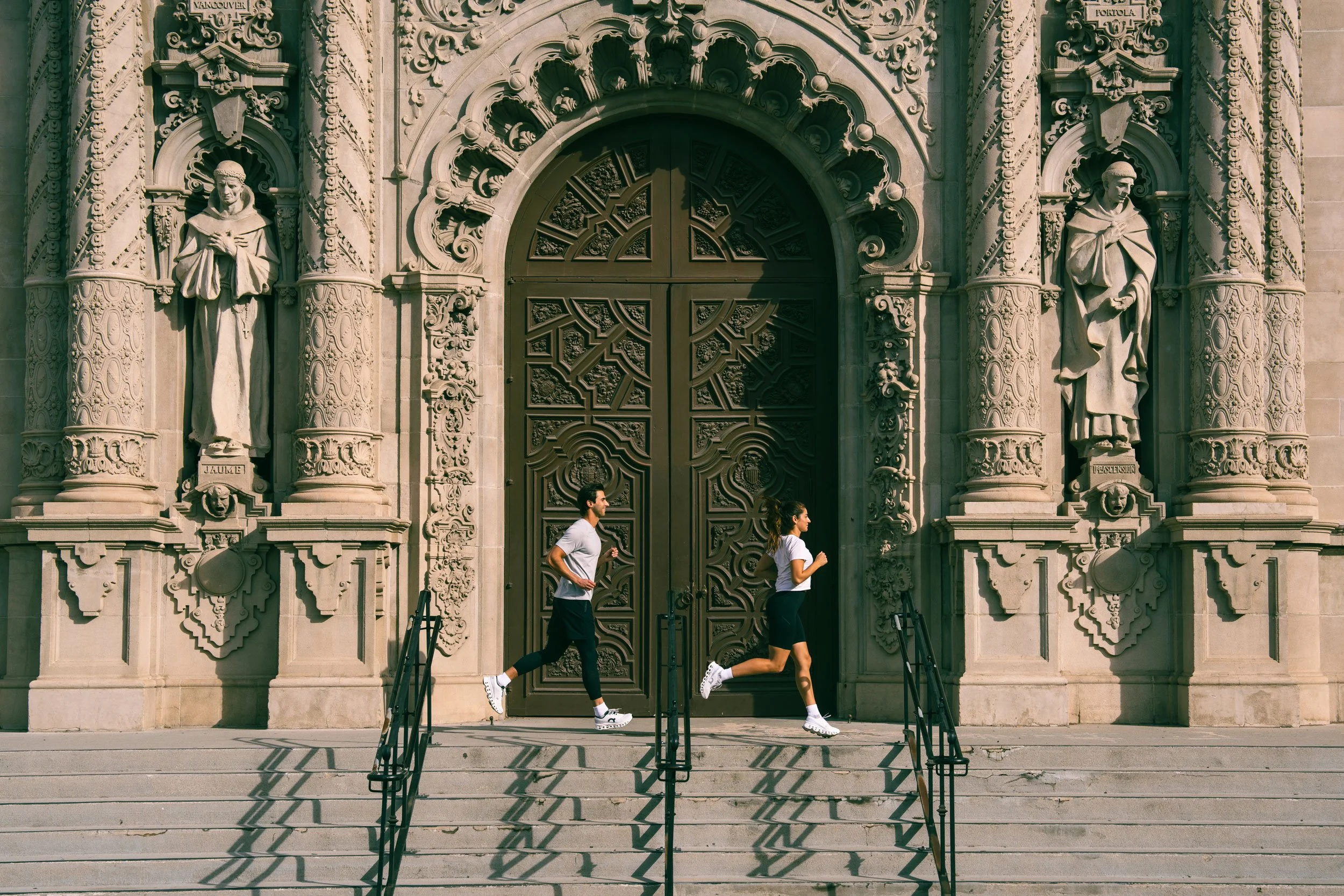 Unretouched lifestyle shot of two people running in front of an ornate historic building with detailed carvings and statues. Road Runner Sports lifestyle image.