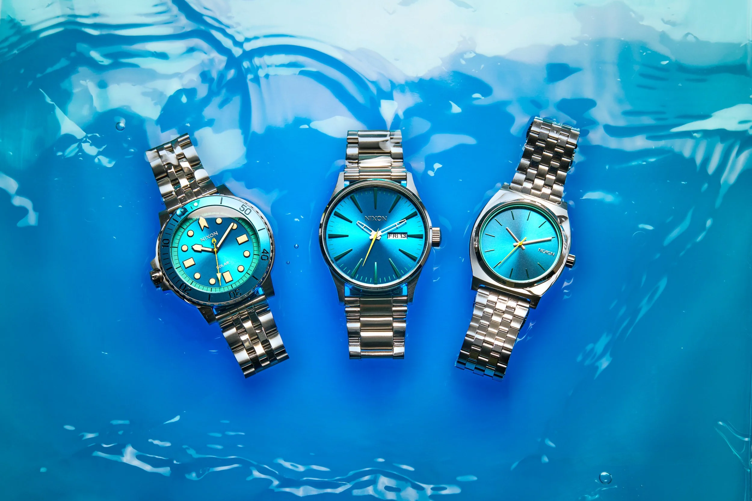 Retouched image of three silver metal wristwatches with blue faces floating on blue water.