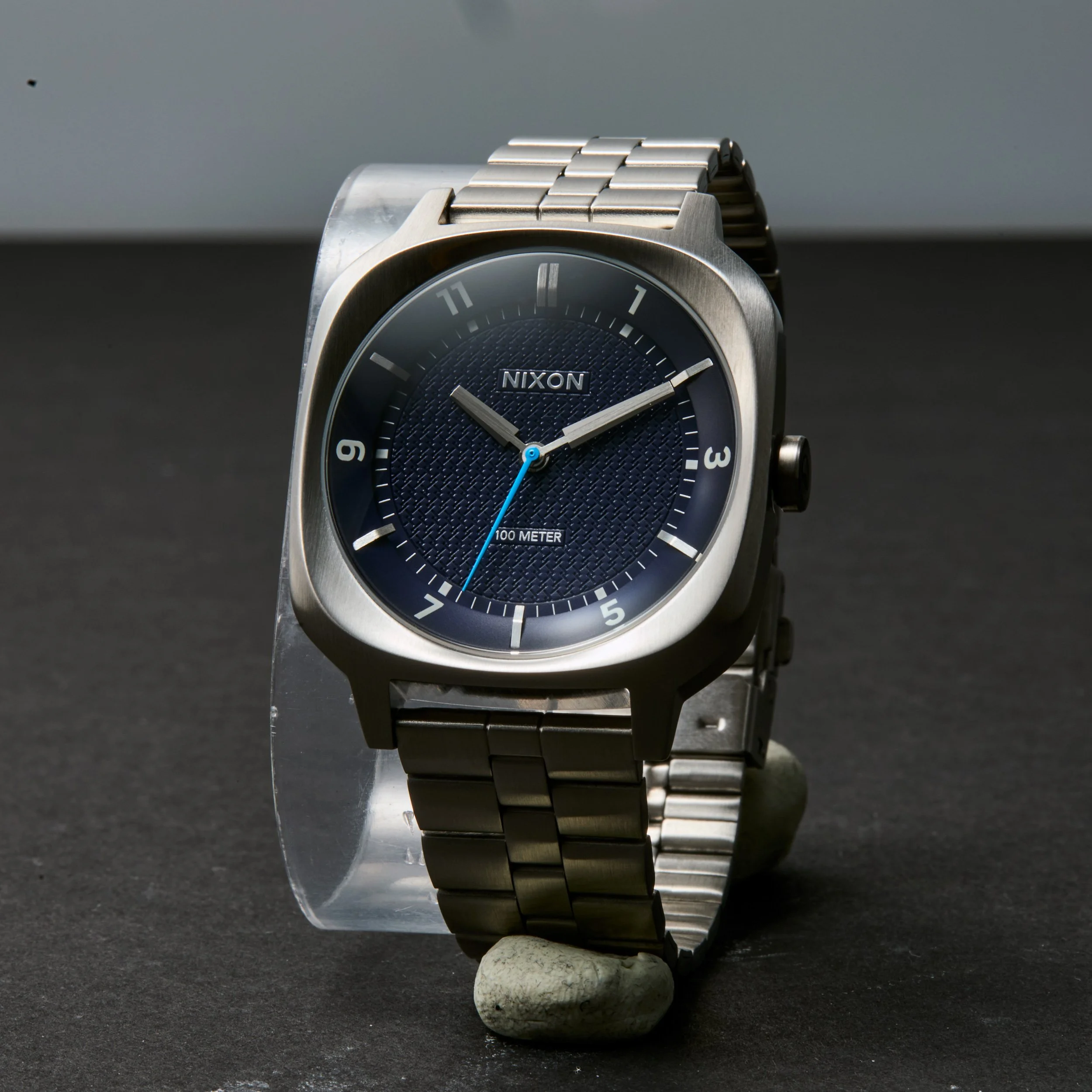 Unretouched product shot of a Nixon wristwatch with a metal band and a dark blue textured dial. Shot to be composited into the AI generated background image and replace the AI generated watch.