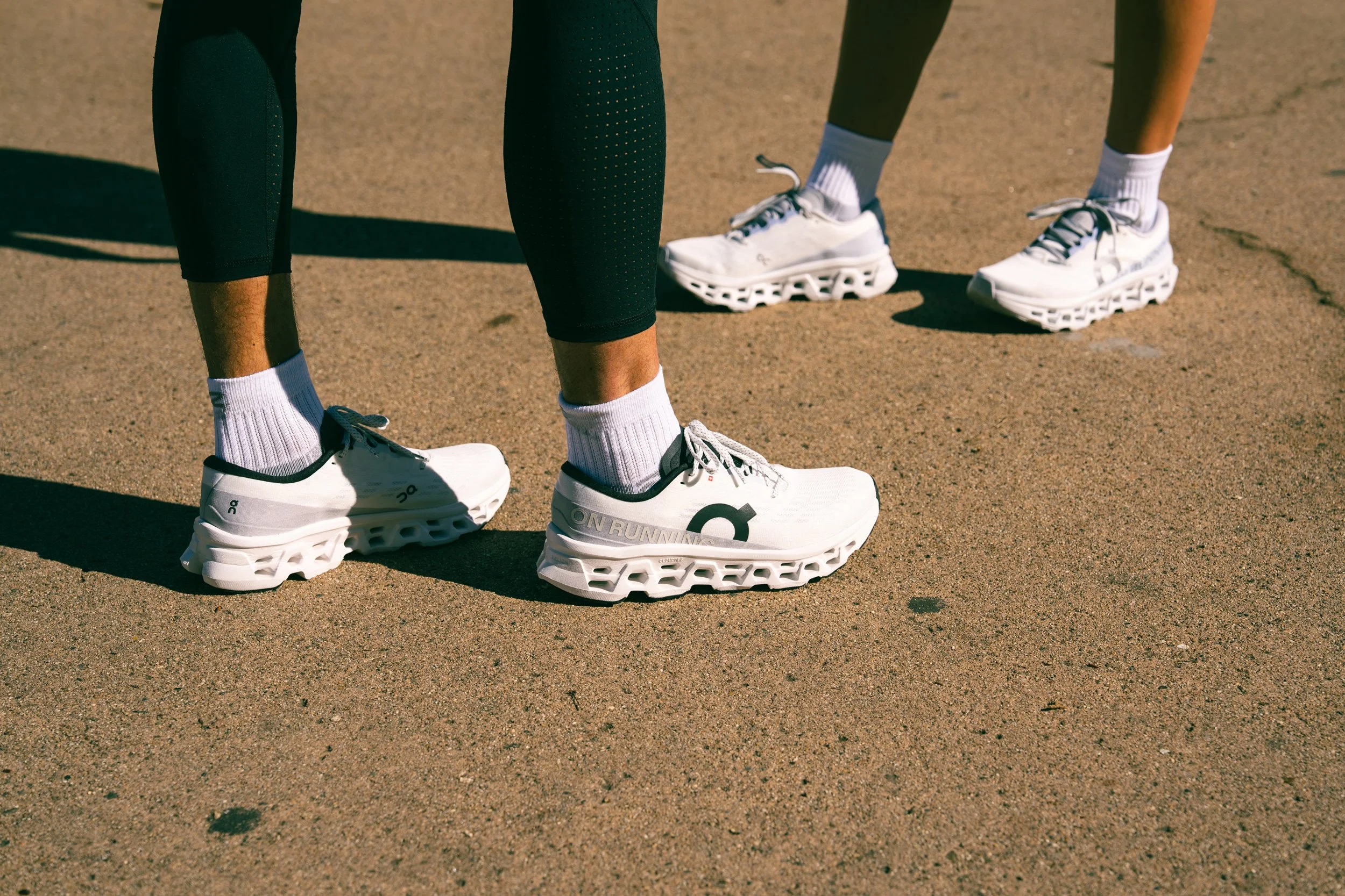 Unretouched close-up of people's legs and feet, wearing On shoes, with focus on white running shoes.