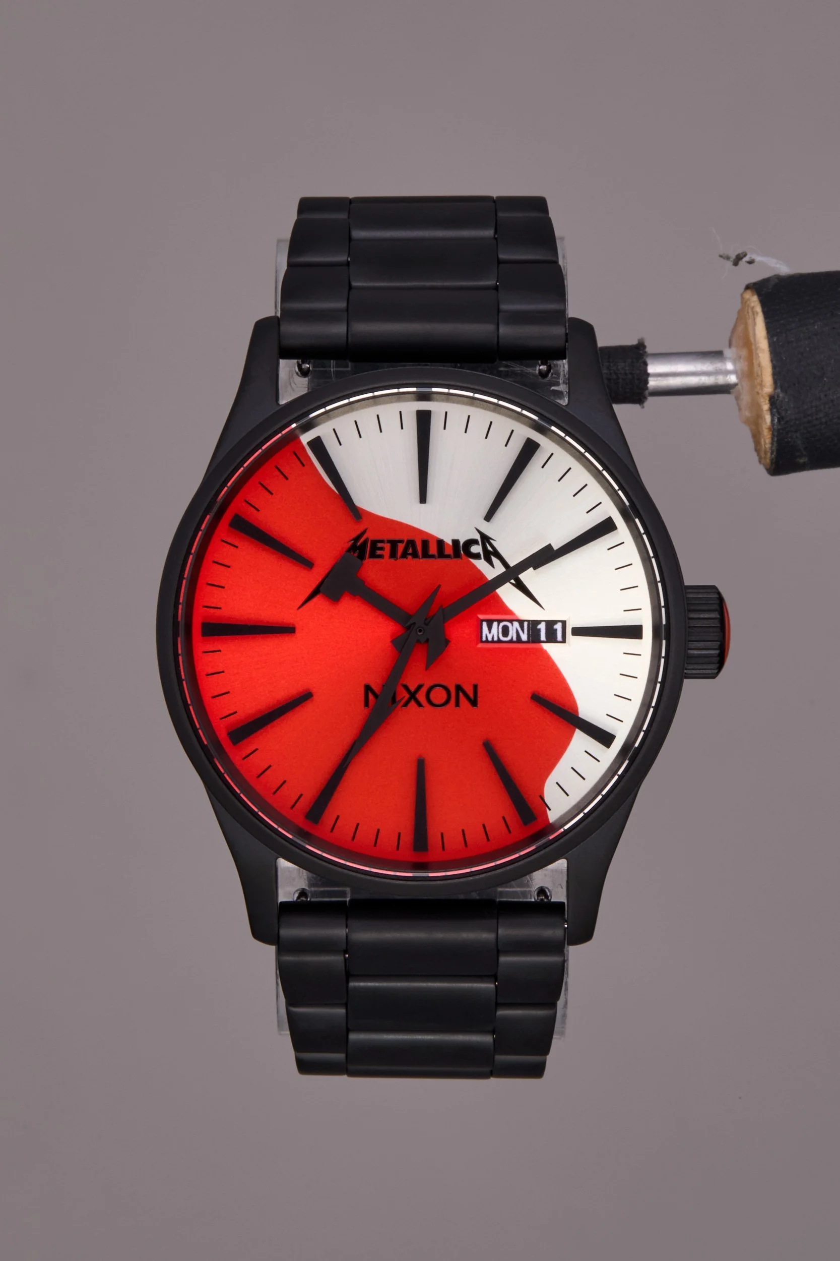 Original shot of a  Nixon wristwatch with a black metal band and a red, white, and black dial. The dial features the Metallica logo.