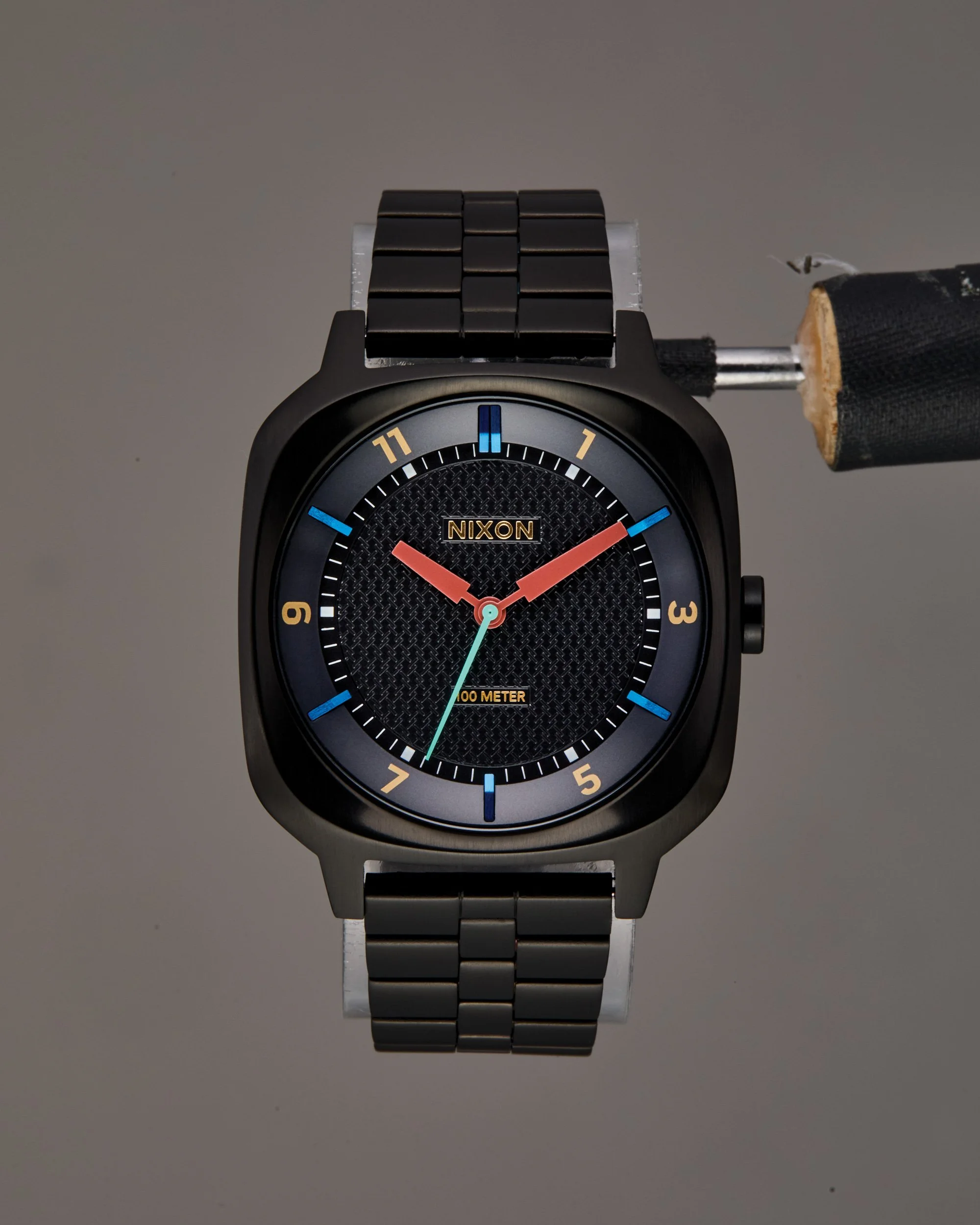 Original e-commerce shot of a black wristwatch with a black band, round face, and gold hour markers, featuring a textured black dial and a small blue second hand.
