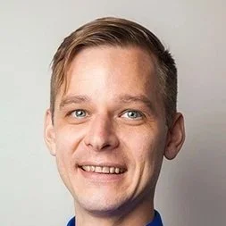 Portrait of a young man with short light brown hair, blue eyes, smiling, wearing a blue shirt.