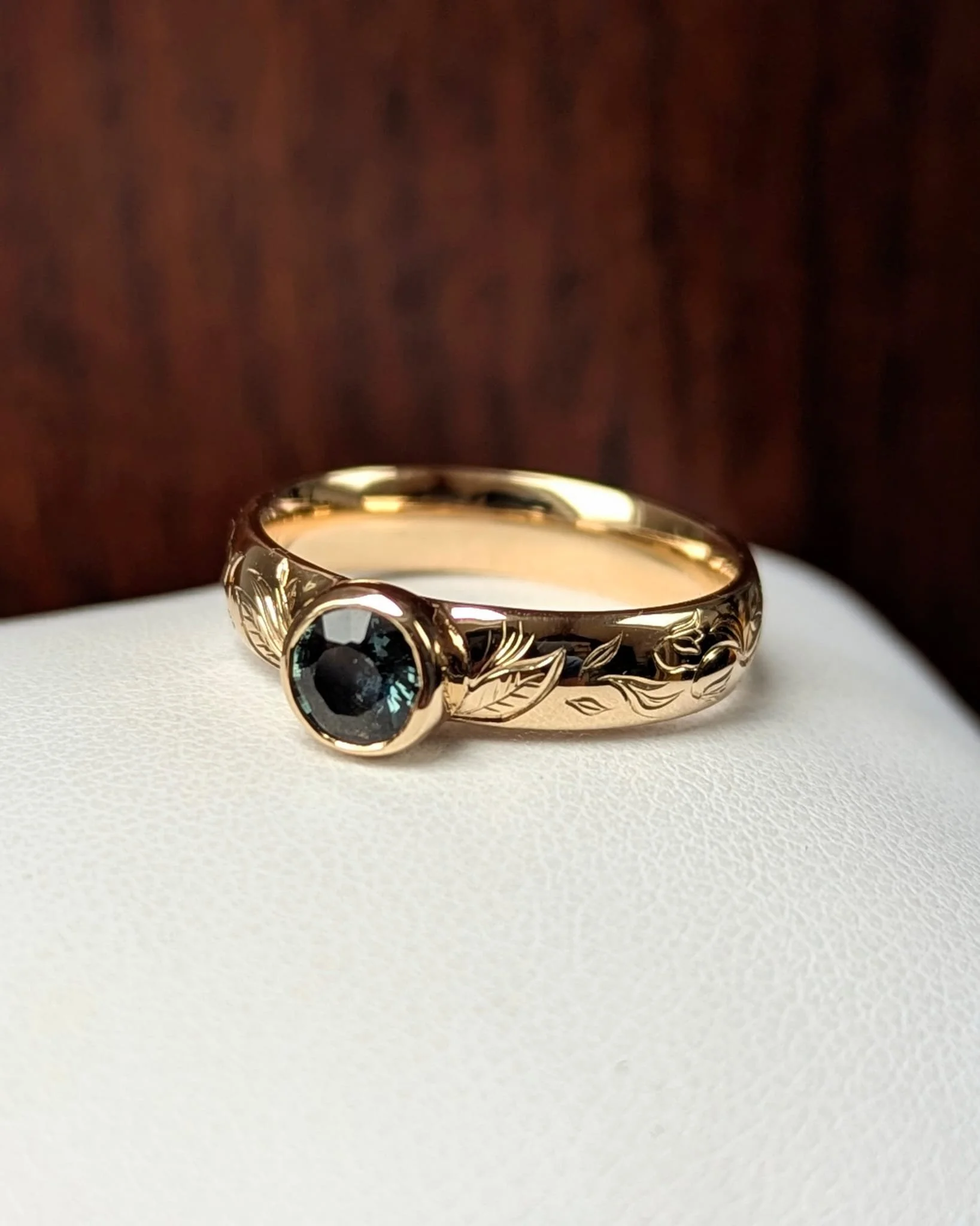 Gold ring with black stone on a white surface, with a dark background.