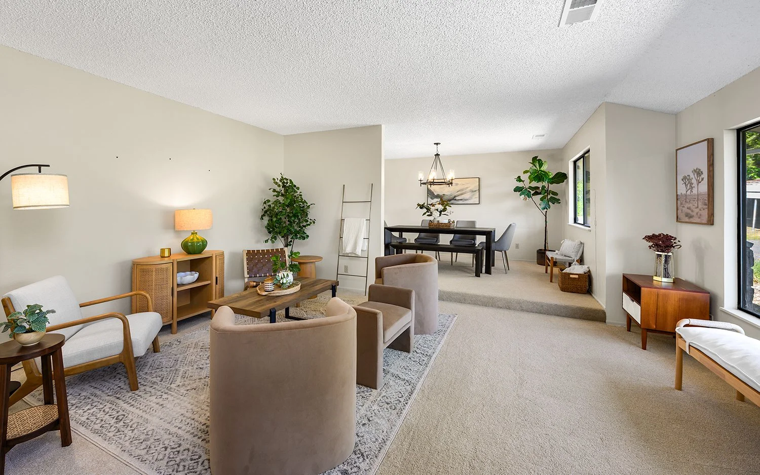 Living and dining room with neutral tones, including a white sofa, armchairs, a wooden coffee table, green plants, a dining table with chairs, and large windows with natural light.