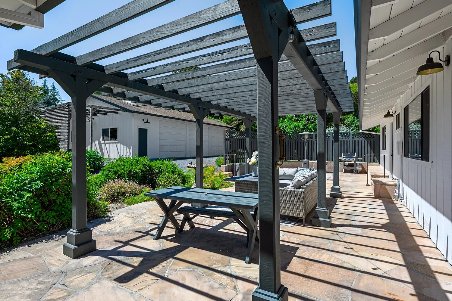 Backyard patio with a wooden pergola, outdoor furniture, a garden, and a detached garage in the background.