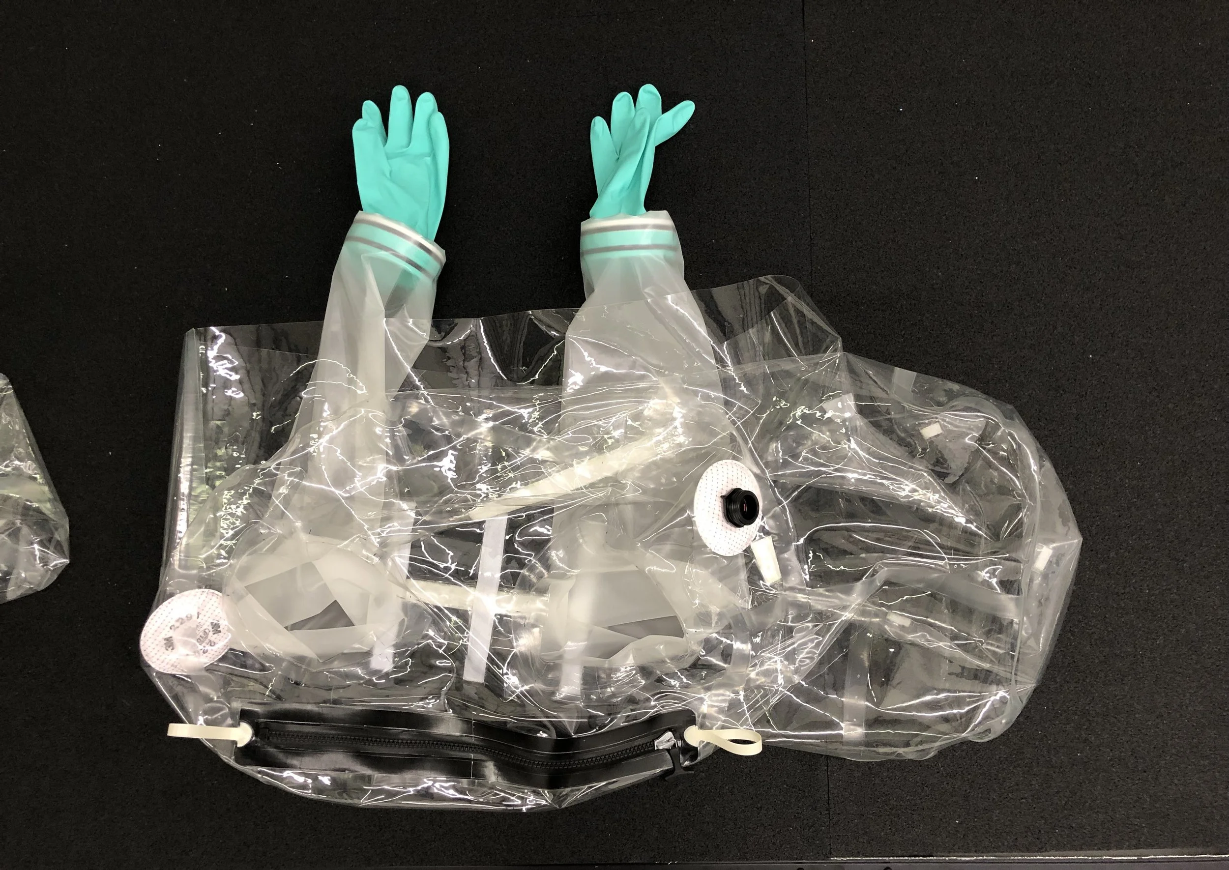 A pair of teal rubber gloves inside a clear plastic bag on a black surface.