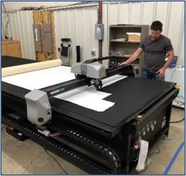 Man operating a large CNC cutting machine for materials and patterns. 