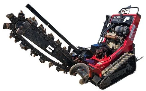 A walk-behind trencher with a red body and black tracks, equipped with a digging chain, used for trenching in soil.