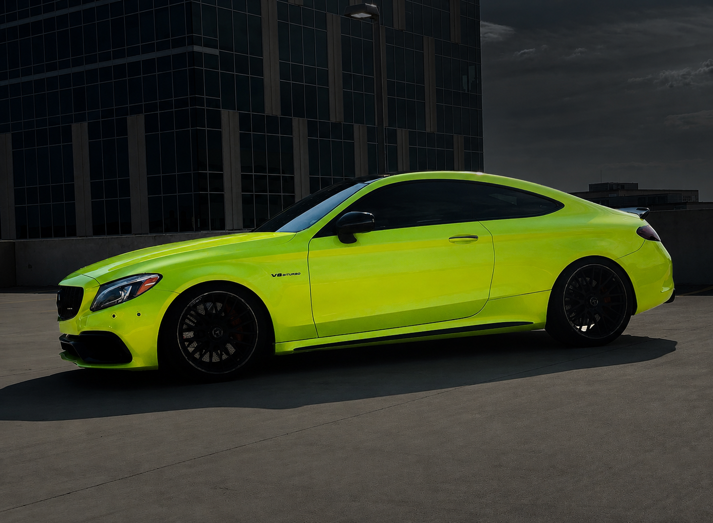 A lime green luxury sports car parked on top of a parking lot with a dark building and cloudy sky in the background.
