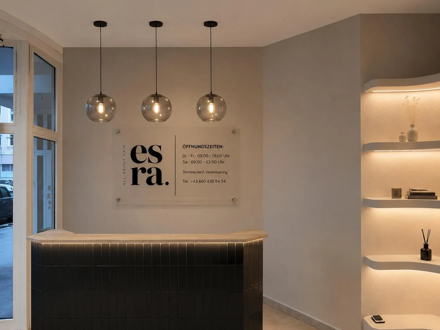 Inneneinrichtung eines Kosmetikstudios mit Empfangstresen, hanging Lamps, Wand mit Text und Regalen, die mit Dekoartikeln dekoriert sind.