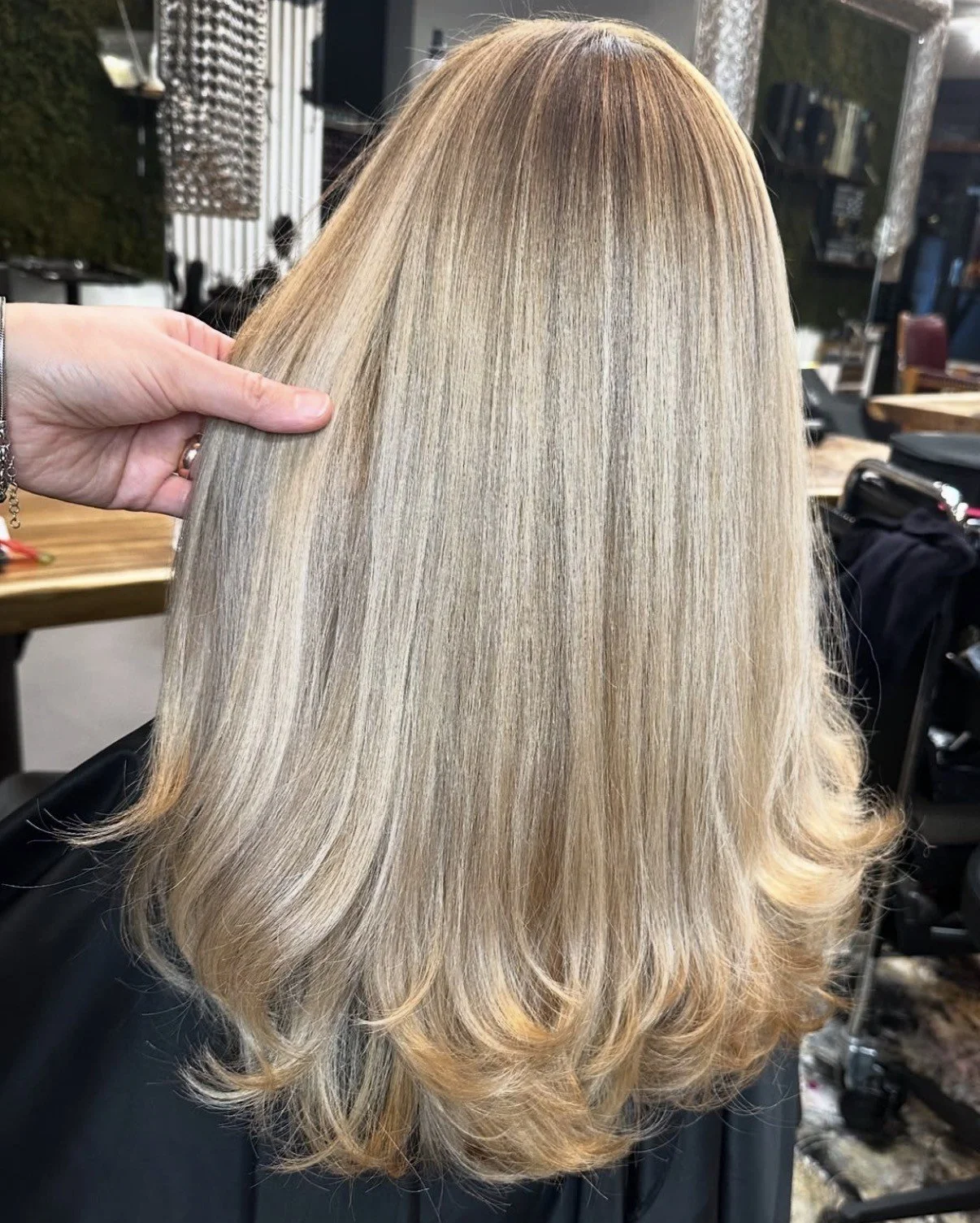 Friseurin präsentiert glattes, blond gefärbtes Haar nach der Coloration im Salon