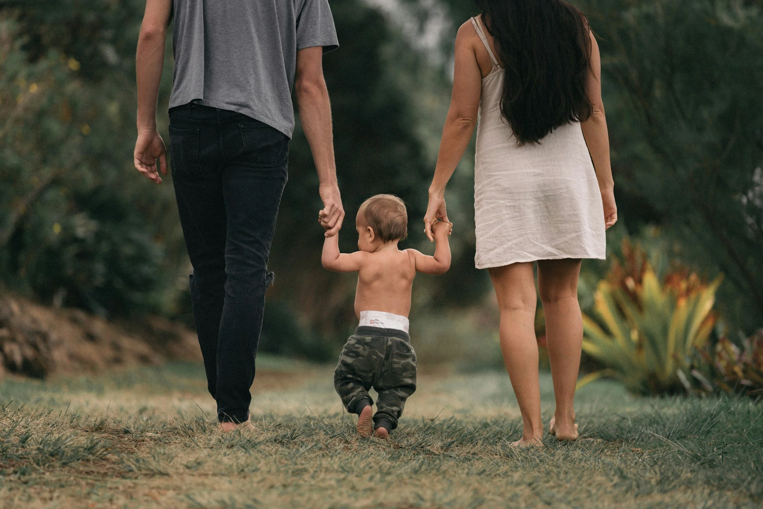 Parents walking hand‑in‑hand with their young son in a grassy outdoor area, reflecting the happy families supported by Divinity Doula in Greenville SC.