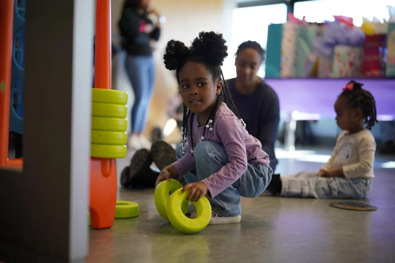 Young girl holding gymnastic rings in a playroom while a nanny‑educator supports structured play and early childhood development.