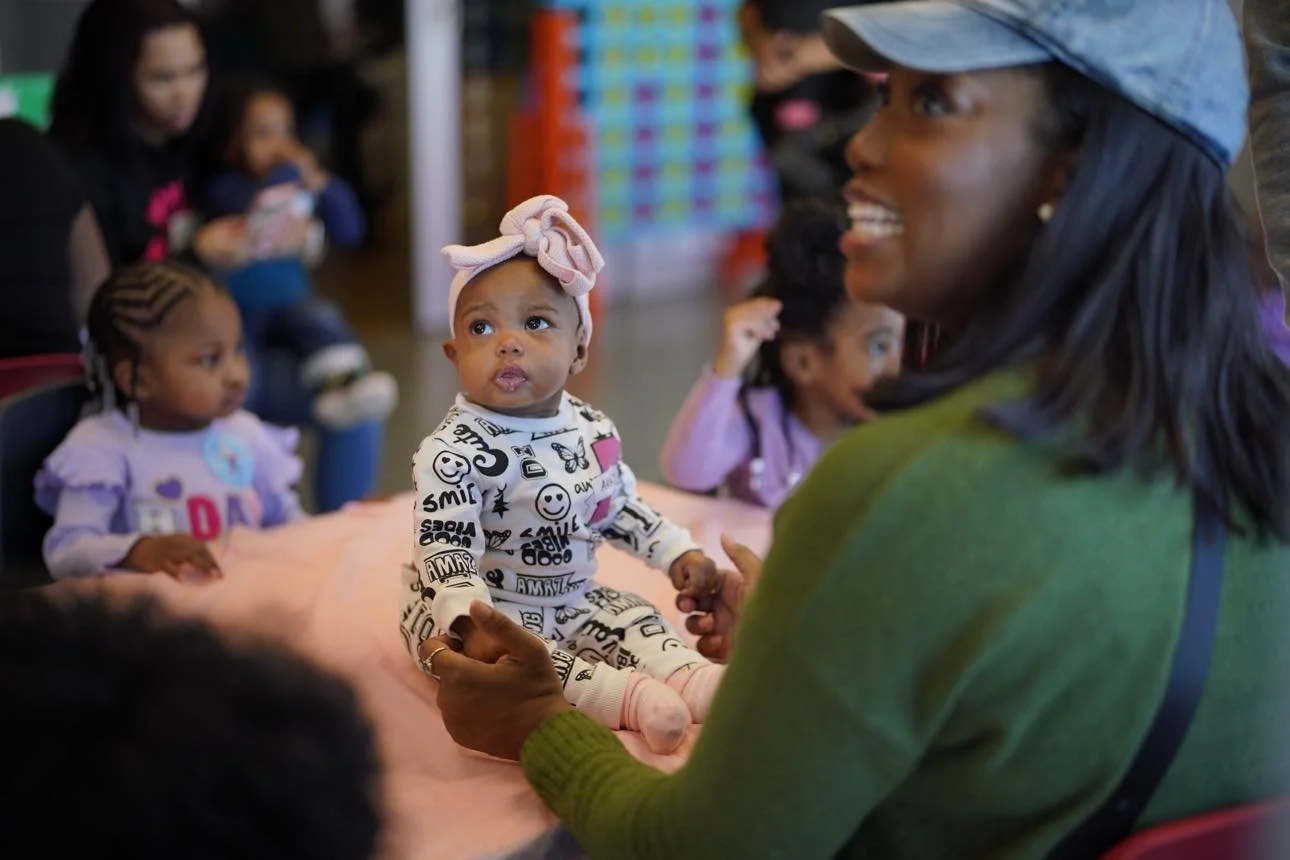 Postpartum doula in Greenville SC with mom holding a baby girl as families gather for a free in‑person Postpartum Power Hour community support event.
