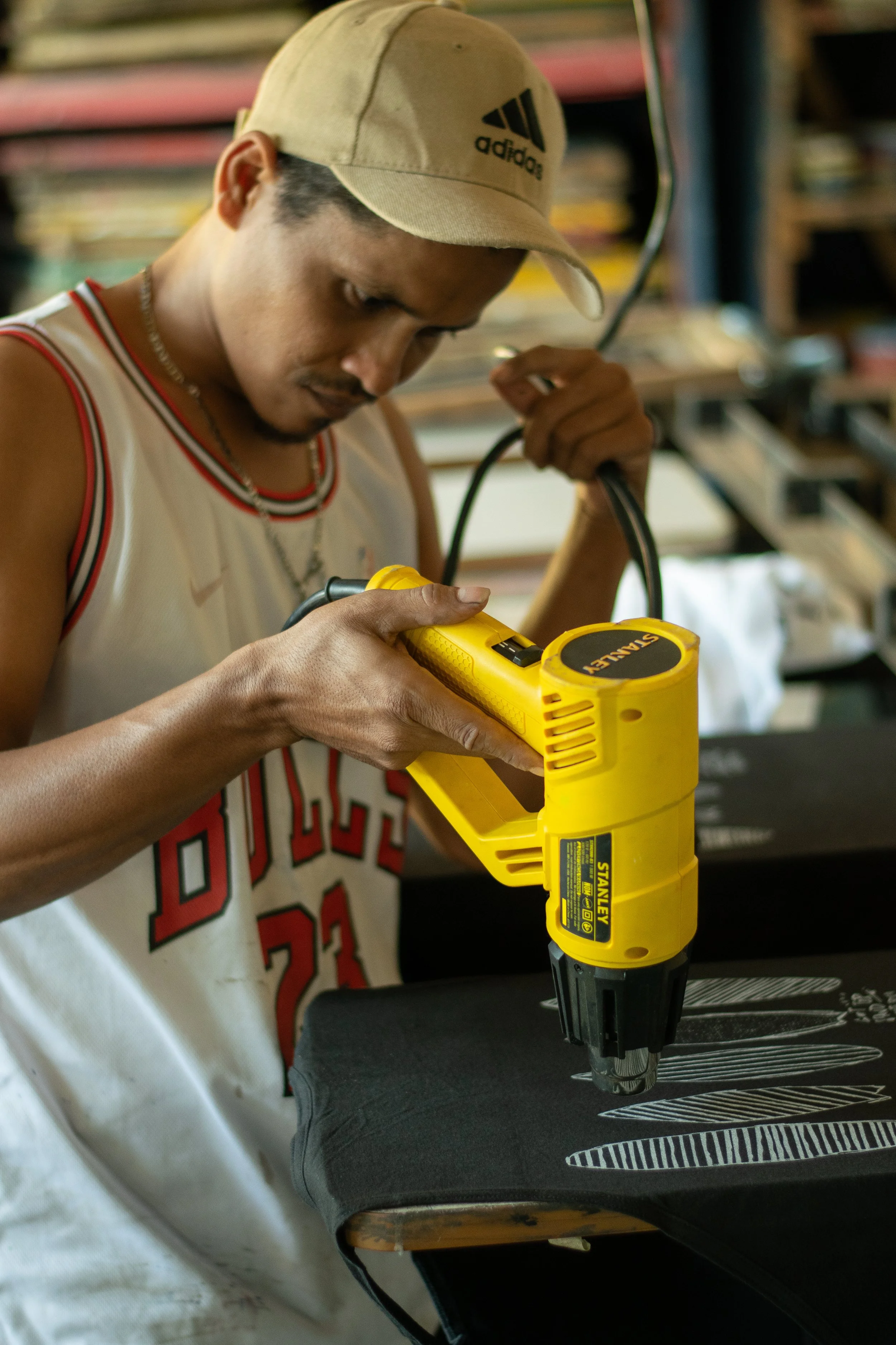 A young man using a yellow Stanley cordless drill on a piece of black material, in a workshop or garage setting.