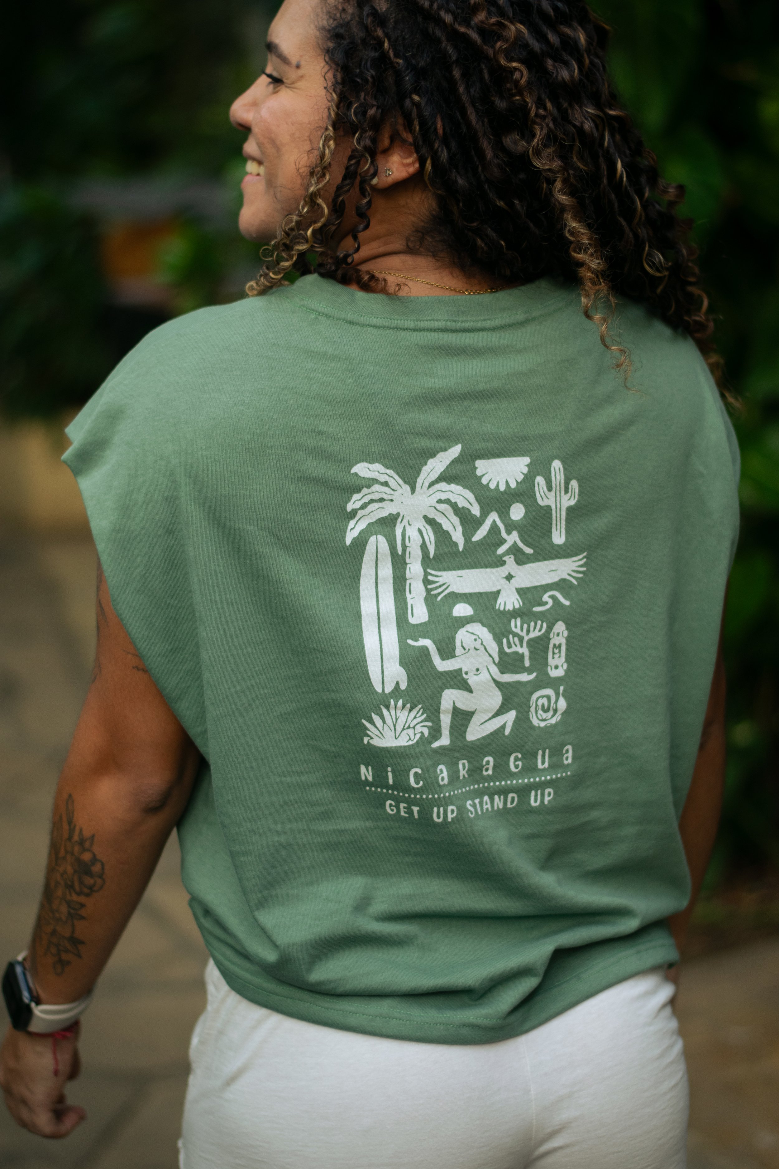 A woman with curly hair wearing a green t-shirt with a Nicaragua theme and white pants.
