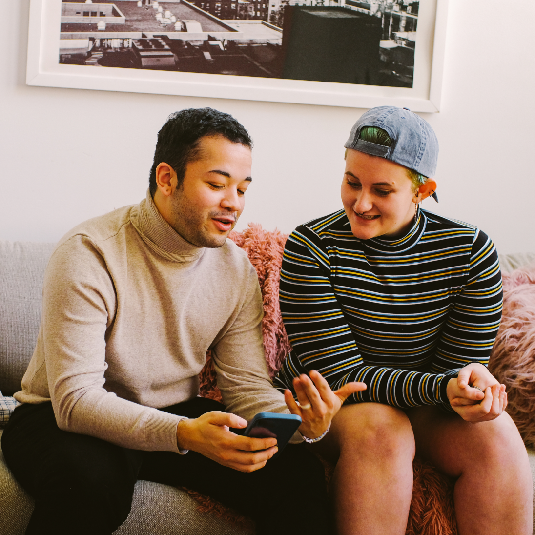 two friends sitting on a couch talking while looking at a phone