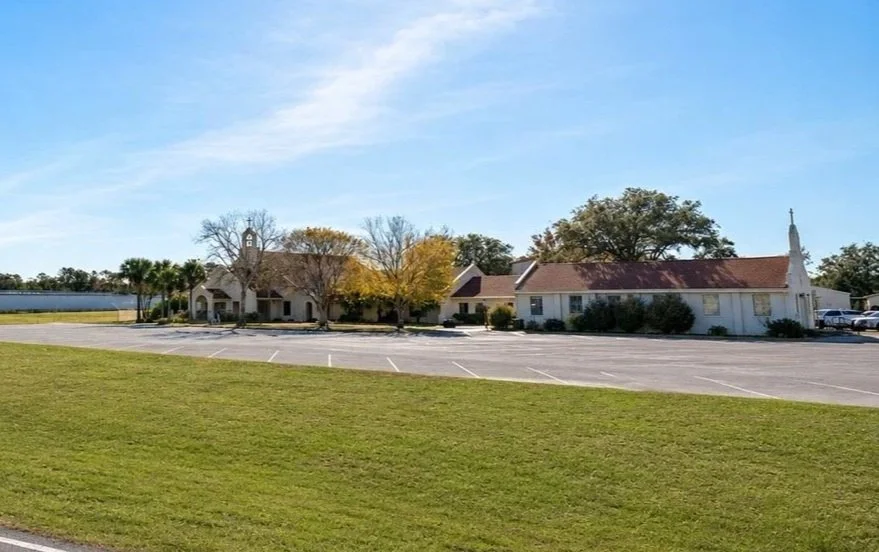 A church surrounded by trees and a large parking lot under a clear blue sky.